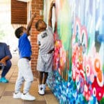 Photo of two boys reaching out to touch a mural while their father watches.